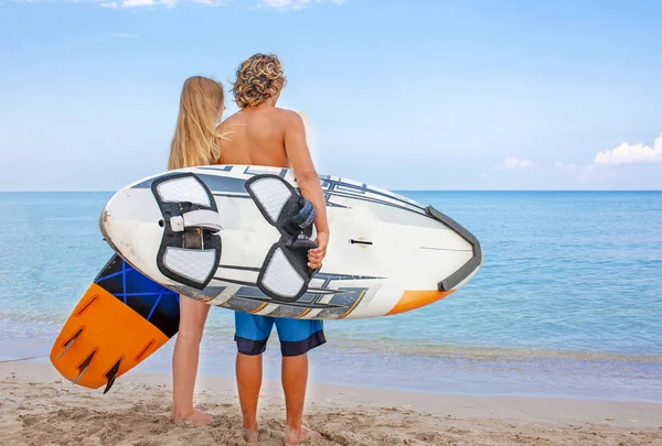 Surfers at the beach- Smiling couple of surfers walking on the beach and having fun in summer. Extreme sport and vacation concept