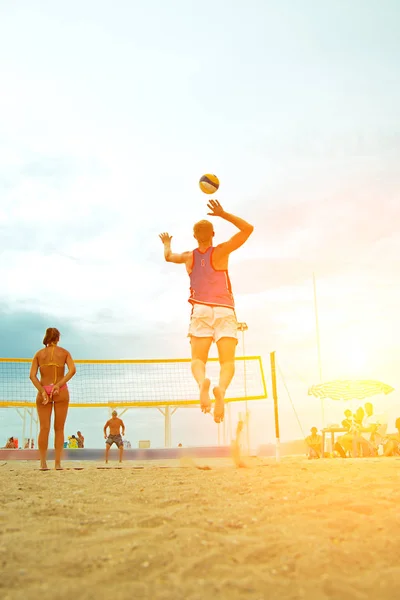 Joueuse de plage de volley-ball est une athlète masculine joueuse de volley-ball se préparant à servir la balle sur la plage et la fille faisant des signes avec ses doigts derrière son dos — Photo