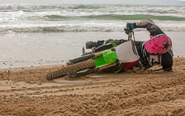 Motorradfahrer stürzte auf einem Motorrad am Strand vor der Kulisse des Meeres — Stockfoto
