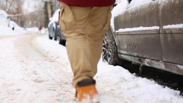 Человек стряхивает снег с ног перед тем, как сесть в машину и уехать. — стоковое видео