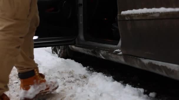 Man schudt uit sneeuw van benen voor zittend in de auto en rijden — Stockvideo