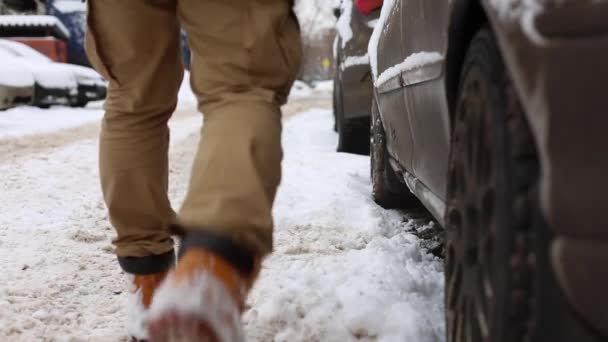 Man shakes off snow from legs before sitting in the car and driving away — ストック動画