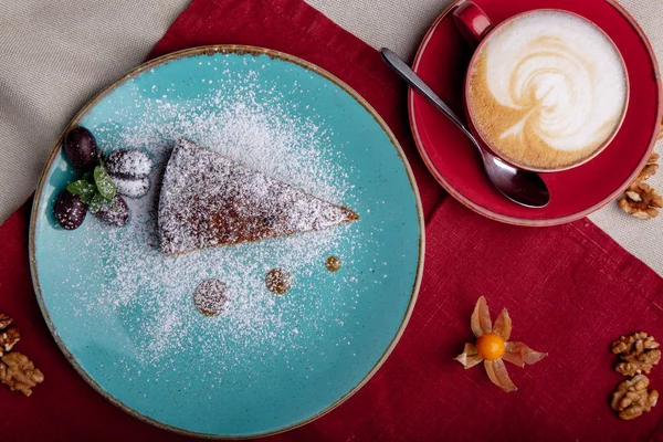 Piece of carrot cake, covered with powdered sugar in a blue plate on a red napkin with cup of coffe and brown sugar