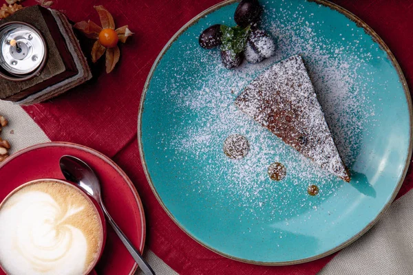 Piece of carrot cake, covered with powdered sugar in a blue plate on a red napkin with cup of coffe and brown sugar