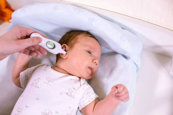 Meettemperatuur babys met contactloze thermometer. Moeder meet de lichaamstemperatuur babys met een thermometer in het oor — Stockfoto