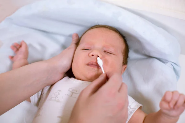 Newborn hygiene. Mother cleaning baby nose with cotton swab, closeup Stock Picture