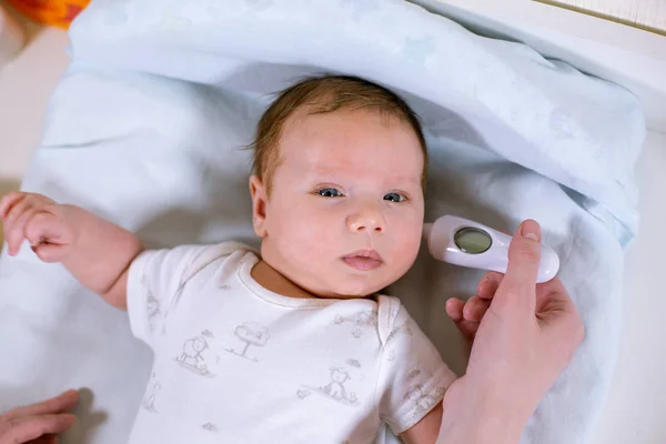 Meettemperatuur babys met contactloze thermometer. Moeder meet de lichaamstemperatuur babys met een thermometer in het oor — Stockfoto