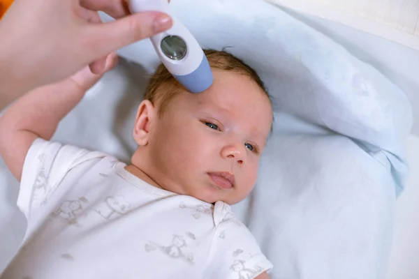 Medir la temperatura de los bebés con termómetro sin contacto. Mamá mide la temperatura corporal de los bebés con un termómetro —  Fotos de Stock