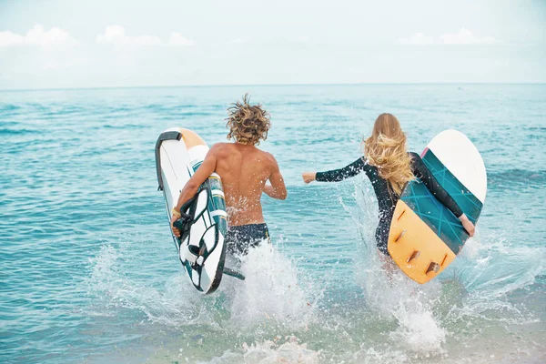 Surfers στο το ζευγάρι παραλία-χαμογελώντας σέρφερ που εκτελούνται στη θάλασσα και έχοντας διασκέδαση το καλοκαίρι. Ακραία έννοια άθλημα και διακοπές — Φωτογραφία Αρχείου