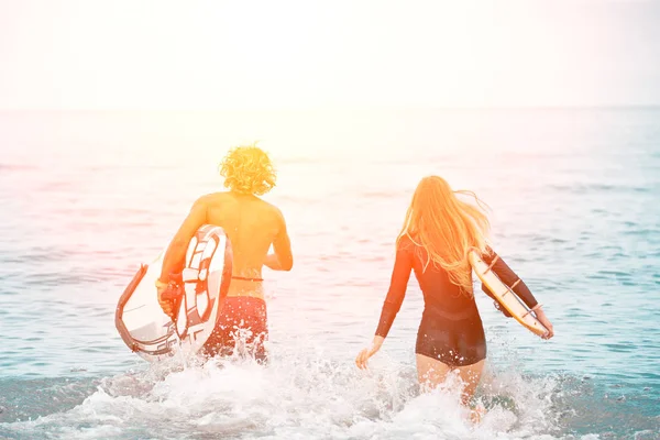 Surfers στο το ζευγάρι παραλία-χαμογελώντας σέρφερ που εκτελούνται στη θάλασσα και έχοντας διασκέδαση το καλοκαίρι. Ακραία έννοια άθλημα και διακοπές — Φωτογραφία Αρχείου