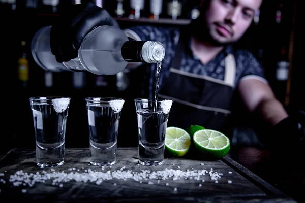 Barman está derramando tequila para os pequenos copos no bar — Fotografia de Stock