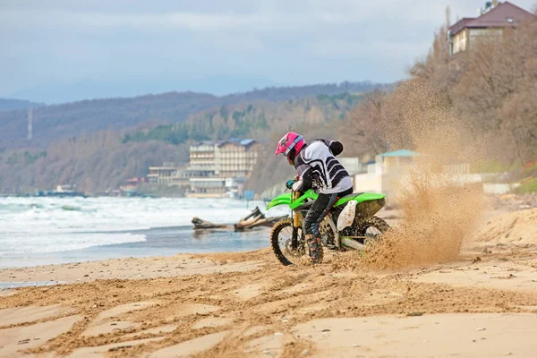 Motorrijder in een beschermend pak een motorfiets rijdt op de zee, spatten vliegen onder de wielen. — Stockfoto