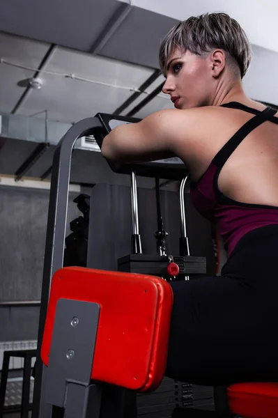 Schöne Sportlerin ist auf einem Simulator in der Turnhalle engagiert. hübsches Mädchen mit der schön angezogenen Figur. Fitness-Mädchen in der Turnhalle — Stockfoto