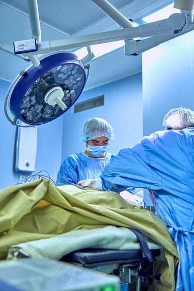 Varios cirujanos que rodean al paciente en la mesa de operaciones durante su trabajo — Foto de Stock