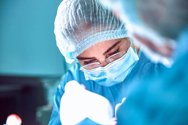 Close up portrait of young female surgeon doctor wearing protective mask and hat during the operation. Healthcare, medical education, surgery concept — Stock Photo, Image