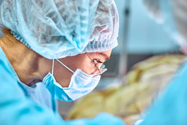 Retrato de cerca de la joven cirujana doctora usando máscara protectora y sombrero durante la operación. Salud, educación médica, concepto de cirugía — Foto de Stock