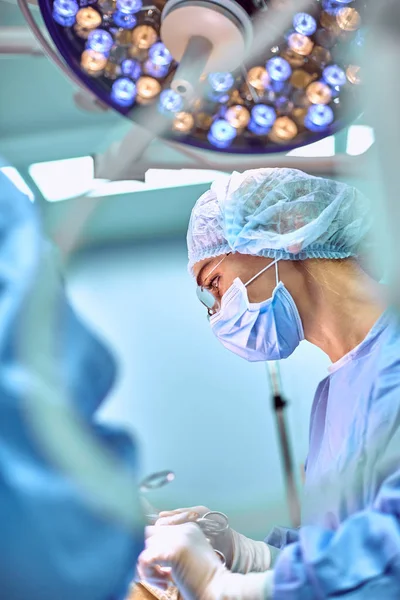 Retrato de cerca de la joven cirujana doctora usando máscara protectora y sombrero durante la operación. Salud, educación médica, concepto de cirugía — Foto de Stock