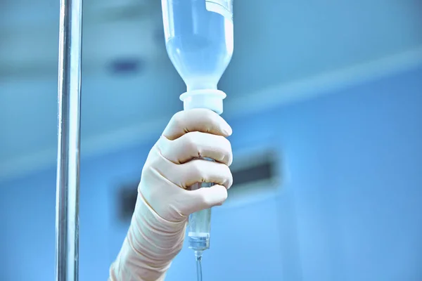 Dropper into a vein close-up on a background of the surgical operational. Doctor woman in sterile gloves sets the drip — Stock Photo, Image