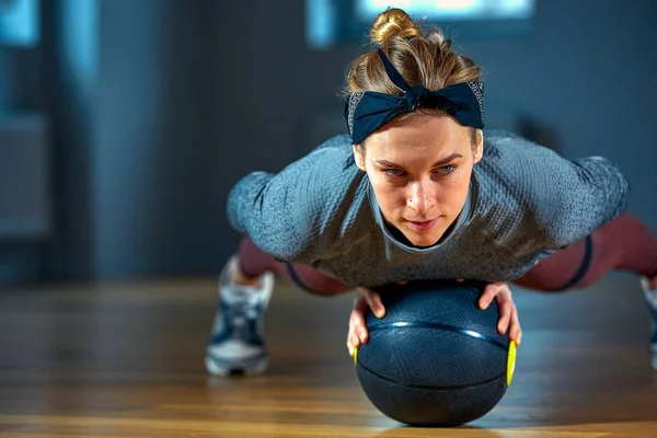 Bela mulher em sportswear posando enquanto sentado no chão com basquete na frente da janela no ginásio Estilo de vida menina saudável e conceito de esporte — Fotografia de Stock