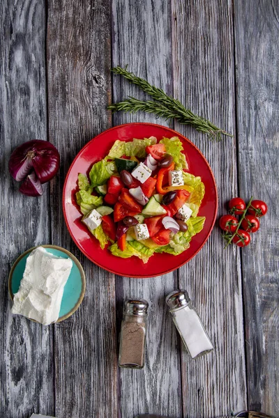 Salada grega de pepino fresco, tomate, pimentão doce, alface, cebola vermelha, queijo feta e azeitonas com azeite sobre fundo de madeira. Alimentos saudáveis — Fotografia de Stock