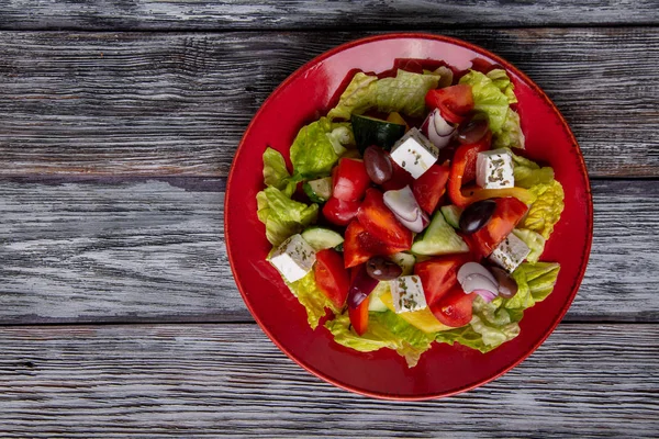 Salada grega de pepino fresco, tomate, pimentão doce, alface, cebola vermelha, queijo feta e azeitonas com azeite sobre fundo de madeira. Alimentos saudáveis — Fotografia de Stock