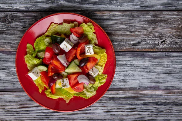 Insalata greca di cetriolo fresco, pomodoro, peperone dolce, lattuga, cipolla rossa, formaggio feta e olive con olio d'oliva su fondo di legno. Cibo sano — Foto Stock