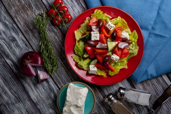 Salada grega de pepino fresco, tomate, pimentão doce, alface, cebola vermelha, queijo feta e azeitonas com azeite sobre fundo de madeira. Alimentos saudáveis — Fotografia de Stock