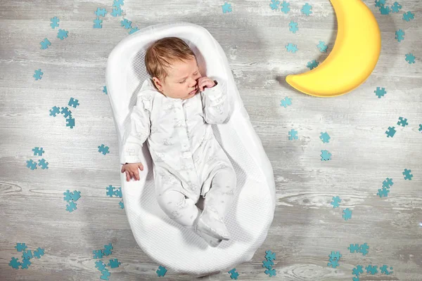 Pasgeboren baby slaapt in een speciale orthopedische matras Baby cocoon, op een houten vloer, speelgoed maan en puzzels rond. Rustig en gezond slapen bij pasgeborenen. — Stockfoto