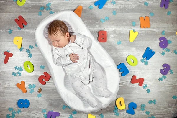 Newborn baby sleeps in a special orthopedic mattress Baby cocoon, on a wooden floor multicolored letters around. Calm and healthy sleep in newborns.