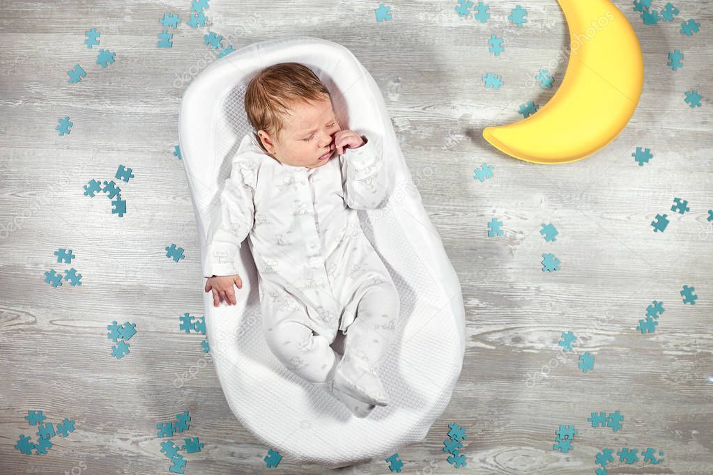 Newborn baby sleeps in a special orthopedic mattress Baby cocoon, on a wooden floor, toy moon and puzzles around. Calm and healthy sleep in newborns.