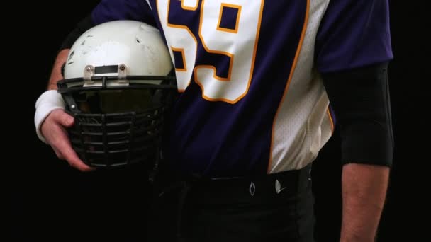 Giocatore di football americano in possesso di un ingranaggio testa contro sfondo nero — Video Stock