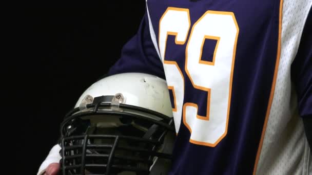 American football player holding a head gear against black background — Stock Video