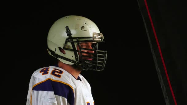 Close up of player of American Football in helmet turns his head to the camera, black background. — Stock Video