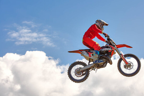Extreme sports background - silhouette of biker jumping on motorbike on sunset, against the blue sky with clouds