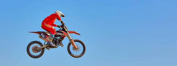 На спортивном фоне - силуэт байкера, прыгающего на мотоцикле на закате, на фоне голубого неба — стоковое фото