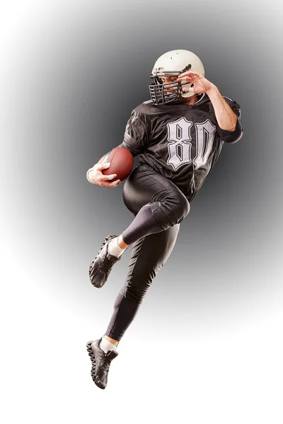 Futbolista americano en uniforme oscuro saltando con pelota sobre fondo gris — Foto de Stock