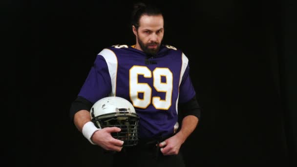 American football. Portrait of an American football player holding a helmet with both hands. An American football player with a helmet in his hands turns to the screen. Preparing for the game — Stock Video