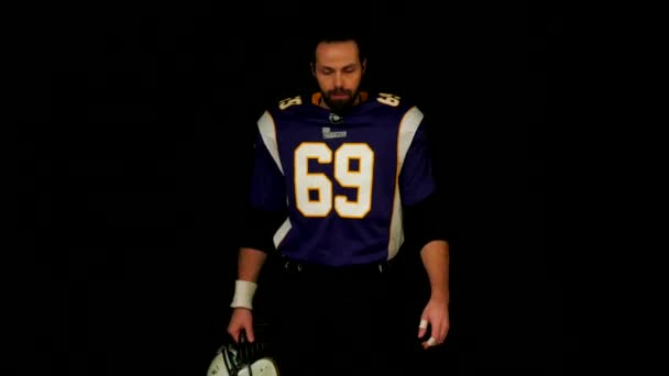 American football player comes out of the dark, concept of appearance on stage, black background. — Stock Video