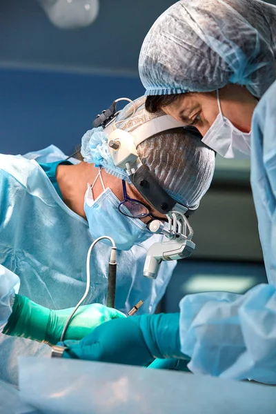 Bir cerrah yakın çekim portresi. Cerrahlar bir hasta üzerinde çalışır. Gergin, ciddi yüzler. Gerçek operasyon. İşletim odada gerilmiş atmosfer. — Stok fotoğraf