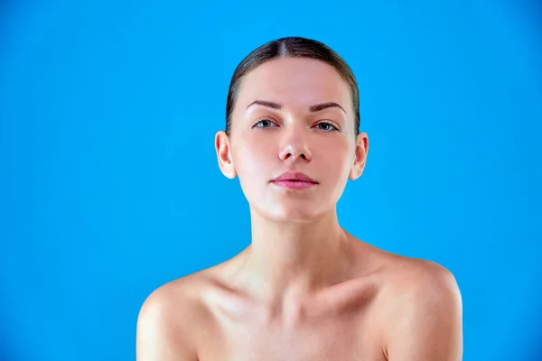 Beauty Woman face Portrait. Beautiful Spa model Girl with Perfect Fresh Clean Skin. Brunette female looking at camera and smiling. Youth and Skin Care Concept.Blue background gray.