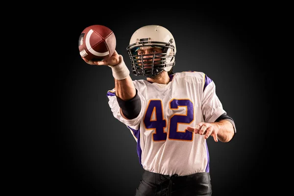 American football player in uniform with the ball is preparing to make a pass. American football concept, black background