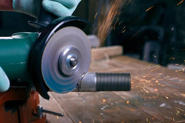 Gloved hands hold an angle grinder and cut the pipe, many sparks fly to the sides — Stock Photo, Image