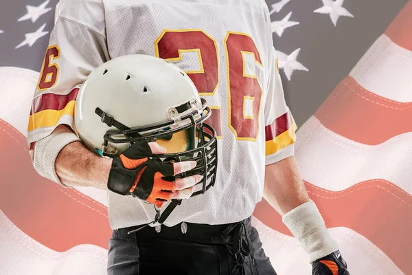 Jugador de fútbol americano con casco en la mano y bandera americana en el fondo . — Foto de Stock