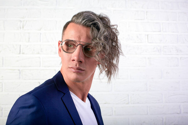Portrait of stylish businessman with curly long hair in sunglasses looks away on white background