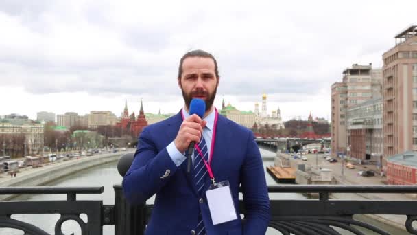 Male reporter with a microphone tells news camera on the background of the city. — Stock Video