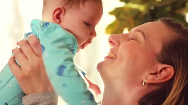 Mother plays with baby in her arms and hugs against window in su ny day — Stock Video