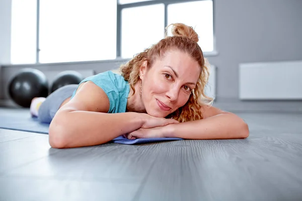 Athletic attractive woman lying on a sports mat in gym. Training concept, sport, workout process
