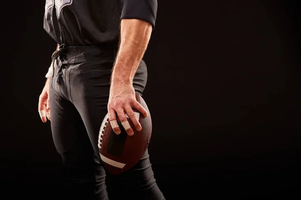 Seção intermediária do jogador de futebol americano com bola contra preto, espaço de cópia, vista lateral — Fotografia de Stock