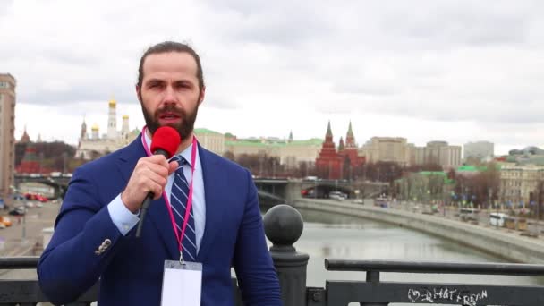 Male reporter with a microphone tells news camera on the background of the city. Russia, Moscow — Stock Video