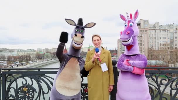 Joven periodista de televisión toma una entrevista de broma una muñeca burros crecimiento en el fondo de la ciudad moderna — Vídeos de Stock